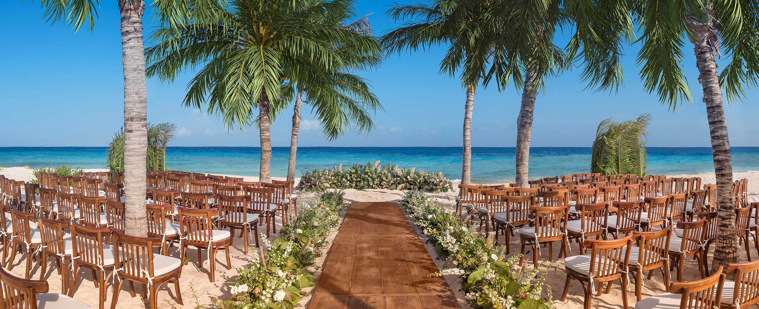 Beach ceremony aisle between palm trees, ocean ahead